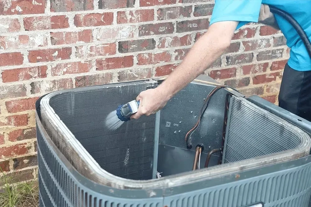 Technician cleaning air conditioning unit with brush against brick wall