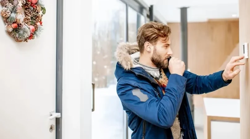 Person in blue winter coat adjusting thermostat near Christmas wreath