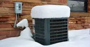 Snow-covered air conditioning unit against brick wall during winter storm