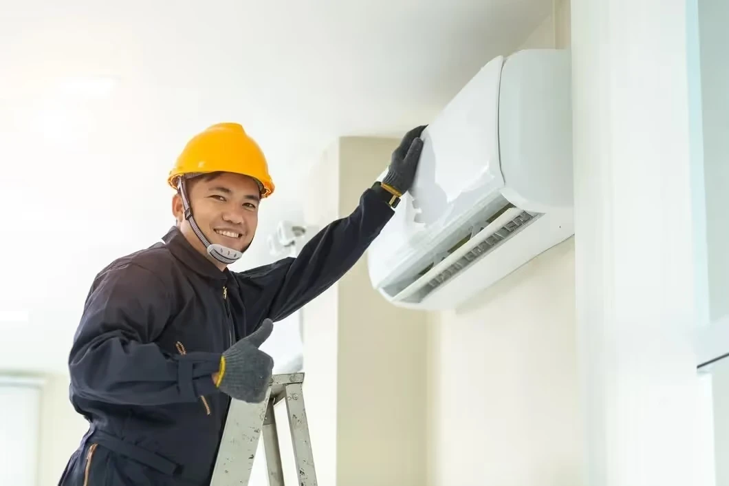 Technician in yellow hard hat installing air conditioning unit on wall