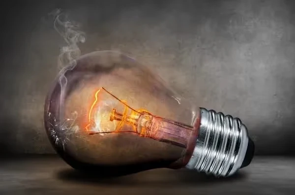 Burning light bulb with glowing filament and smoke on dark background