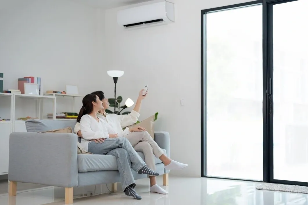  A woman on a sofa pointing a remote at a wall-mounted AC unit.