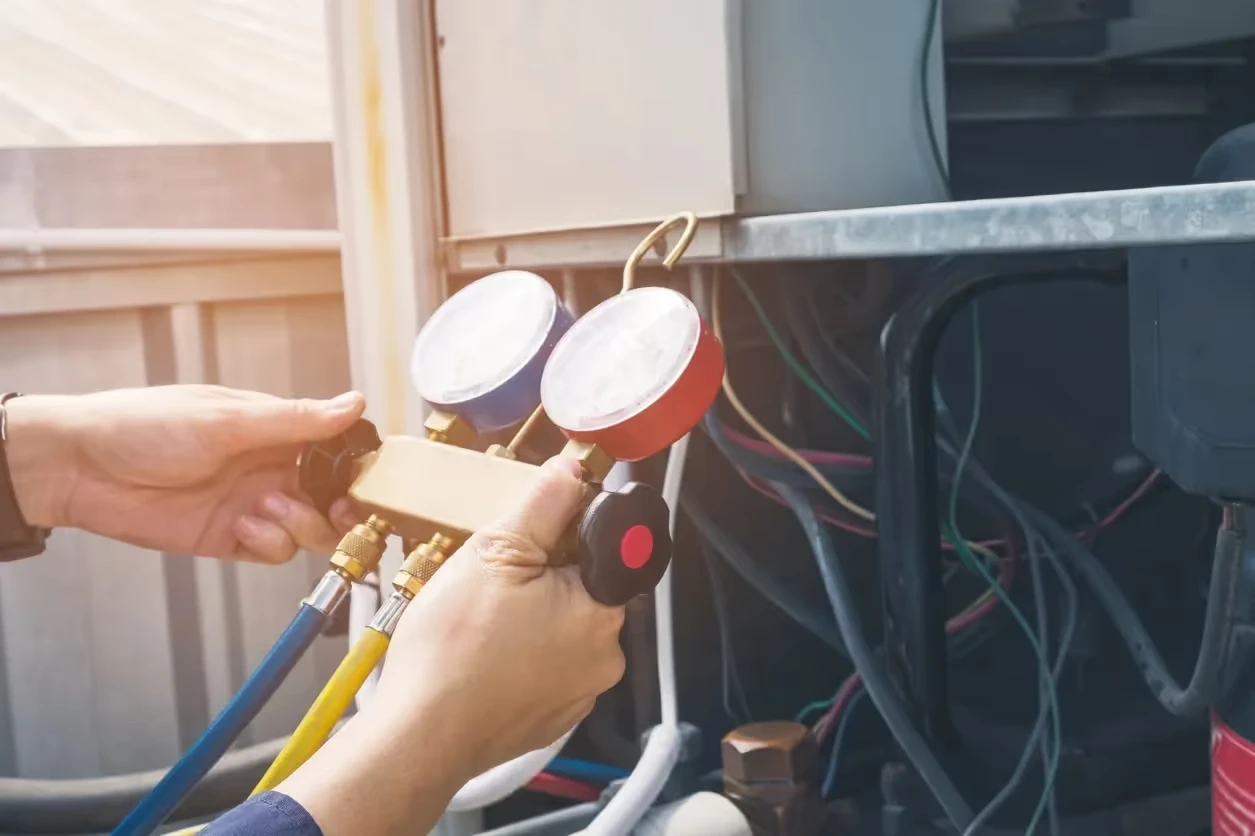 Technician checking pressure gauges on HVAC system electrical connections