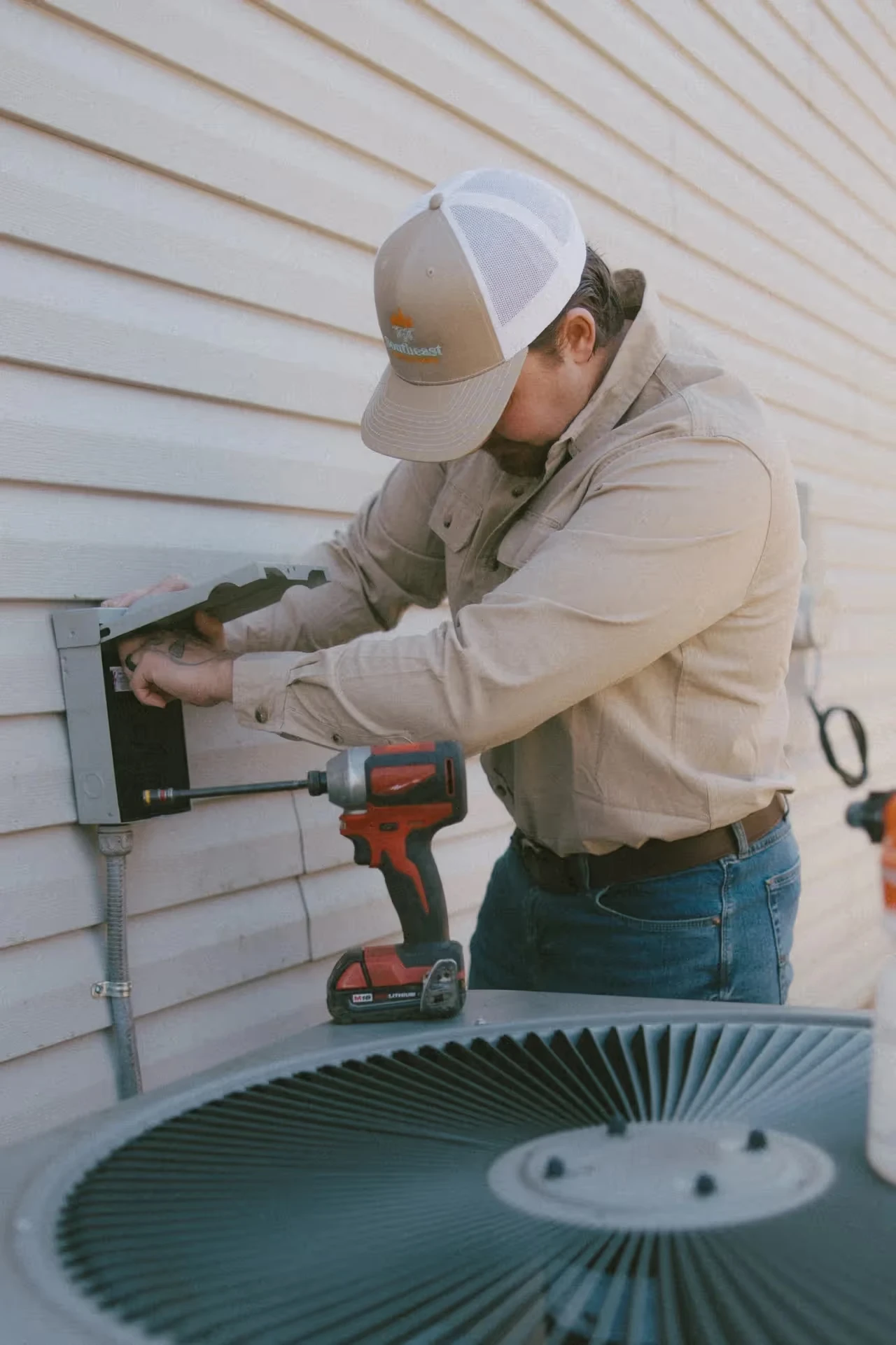 Technician repairing air conditioning unit with drill on exterior wall