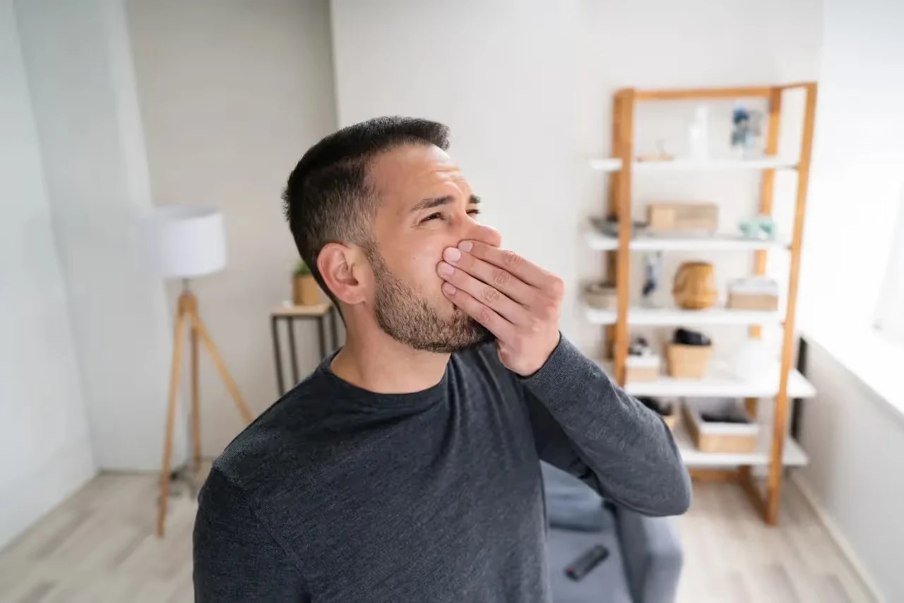 Tired man yawning and covering mouth in minimalist home interior