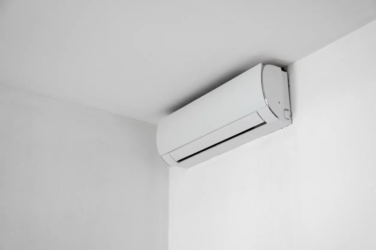 Technician in orange shirt installing or servicing a white wall-mounted air conditioner