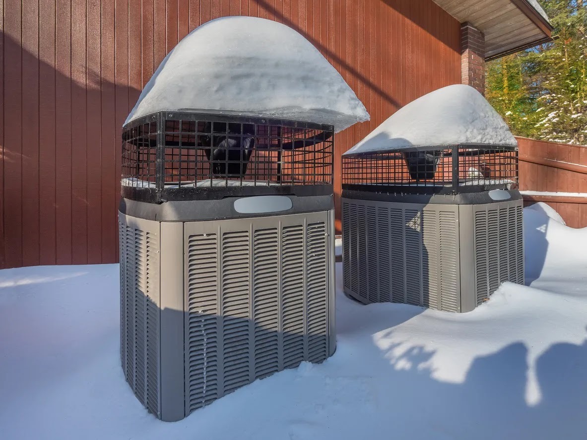 Two snow-covered air conditioning units outside a wooden building