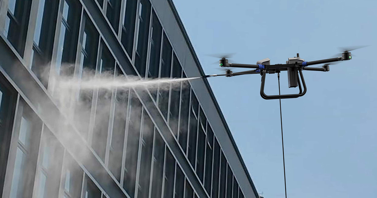 Drone spraying mist on the side of a multi-story glass building against blue sky.
