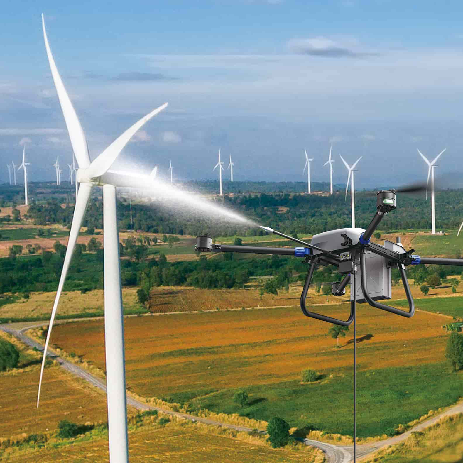 Drone spraying a liquid onto a wind turbine in a large wind farm with green and brown fields.
