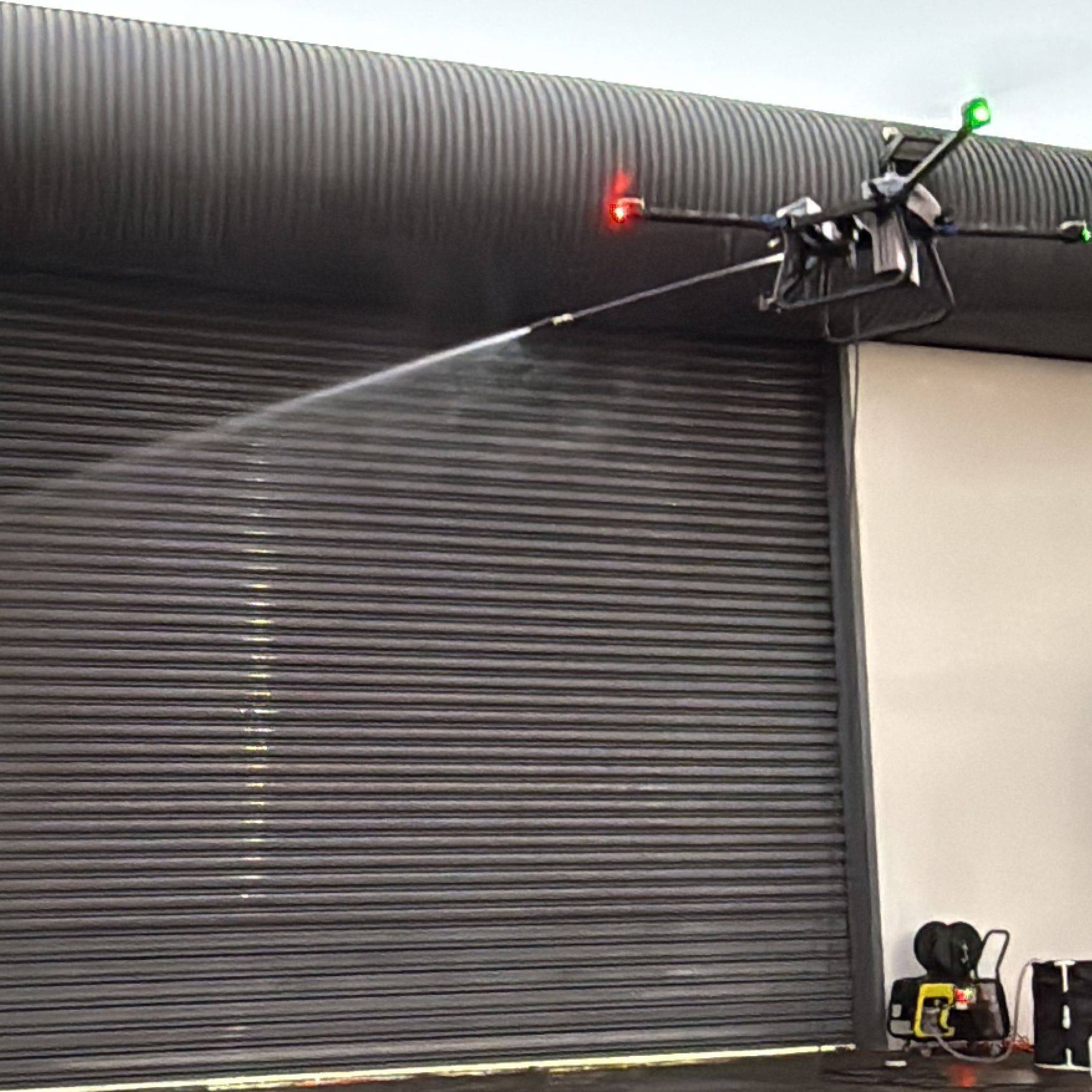 Drone spraying water on a large closed industrial roller door.