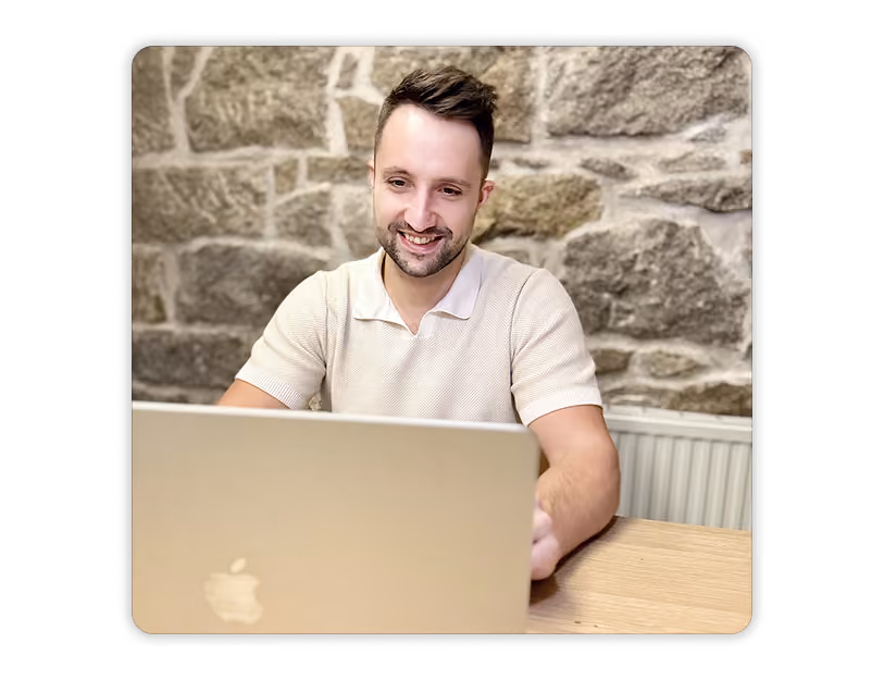 Timo, einer der Geschäftsführer lächelt und führt ein online Geschäftsmeeting an einem Laptop vor einer Steinwand.