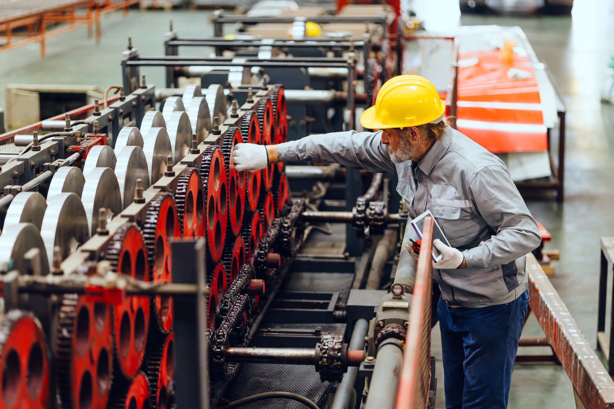 Technician in a hard hat inspecting rolling machinery on a plant floor