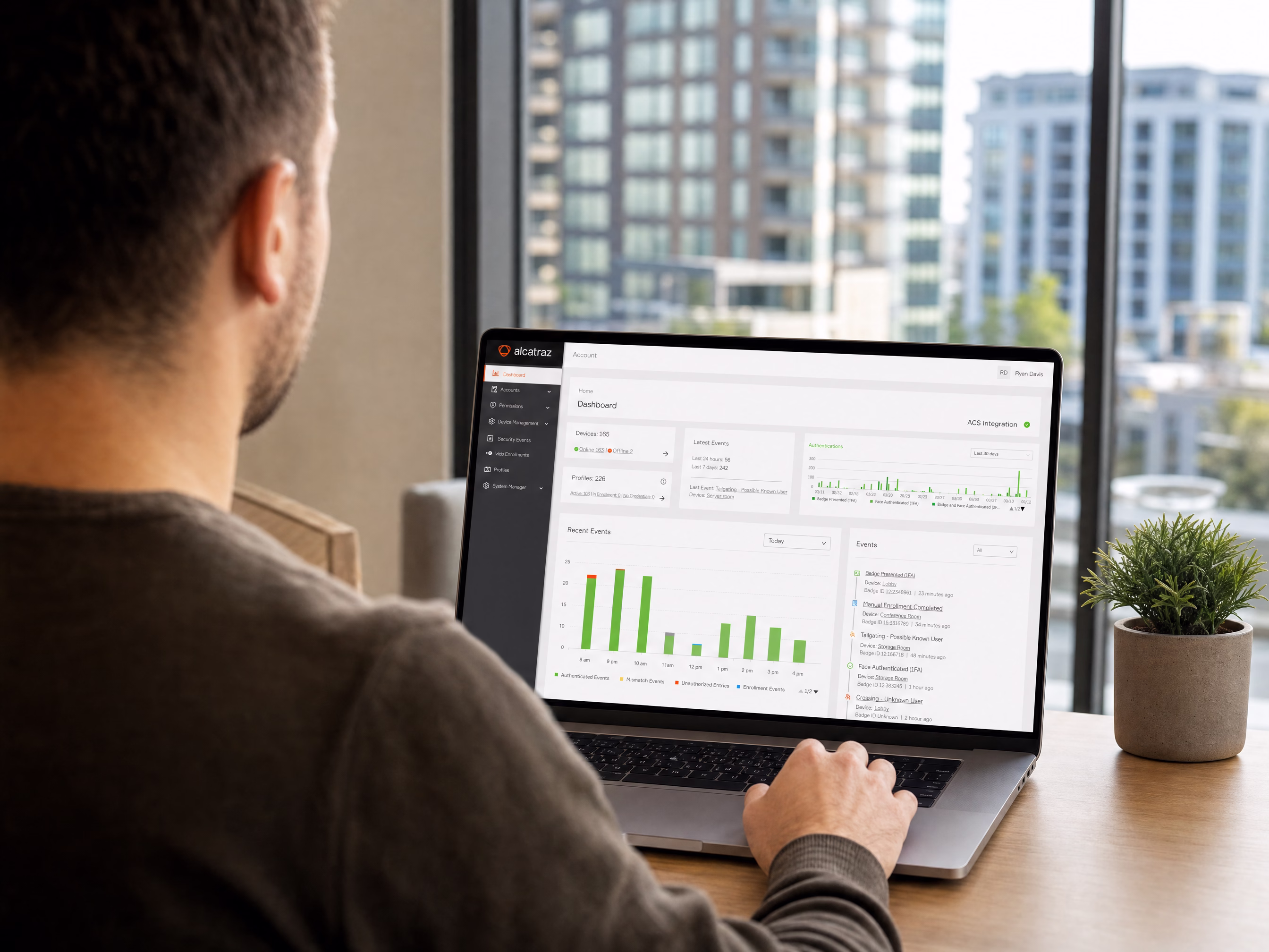 A property manager reviewing the Rock Cortex dashboard on a laptop, city towers visible through the window
