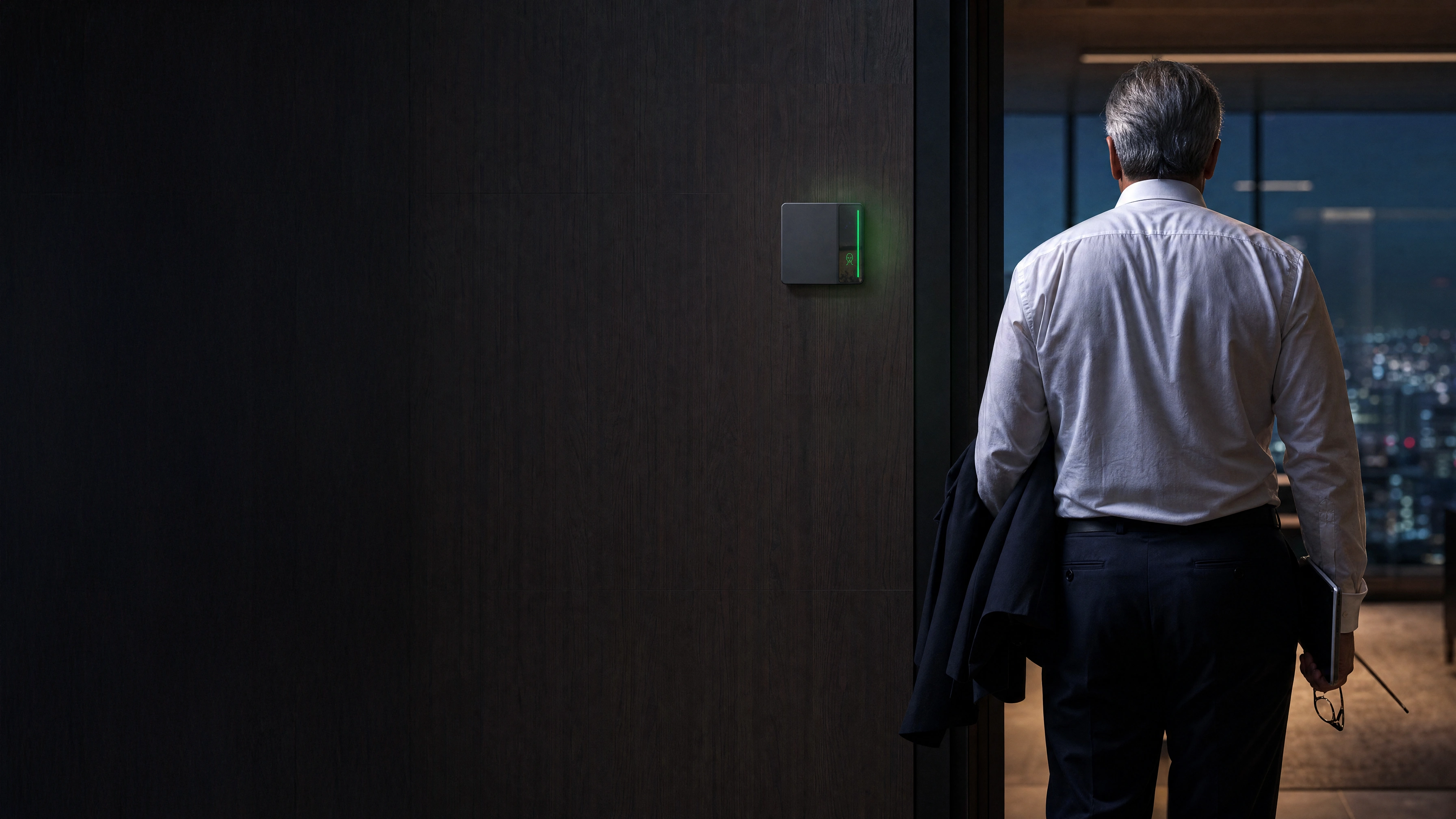 An executive walking through a dark wood executive-floor doorway at night as the Rock reader light bar turns green