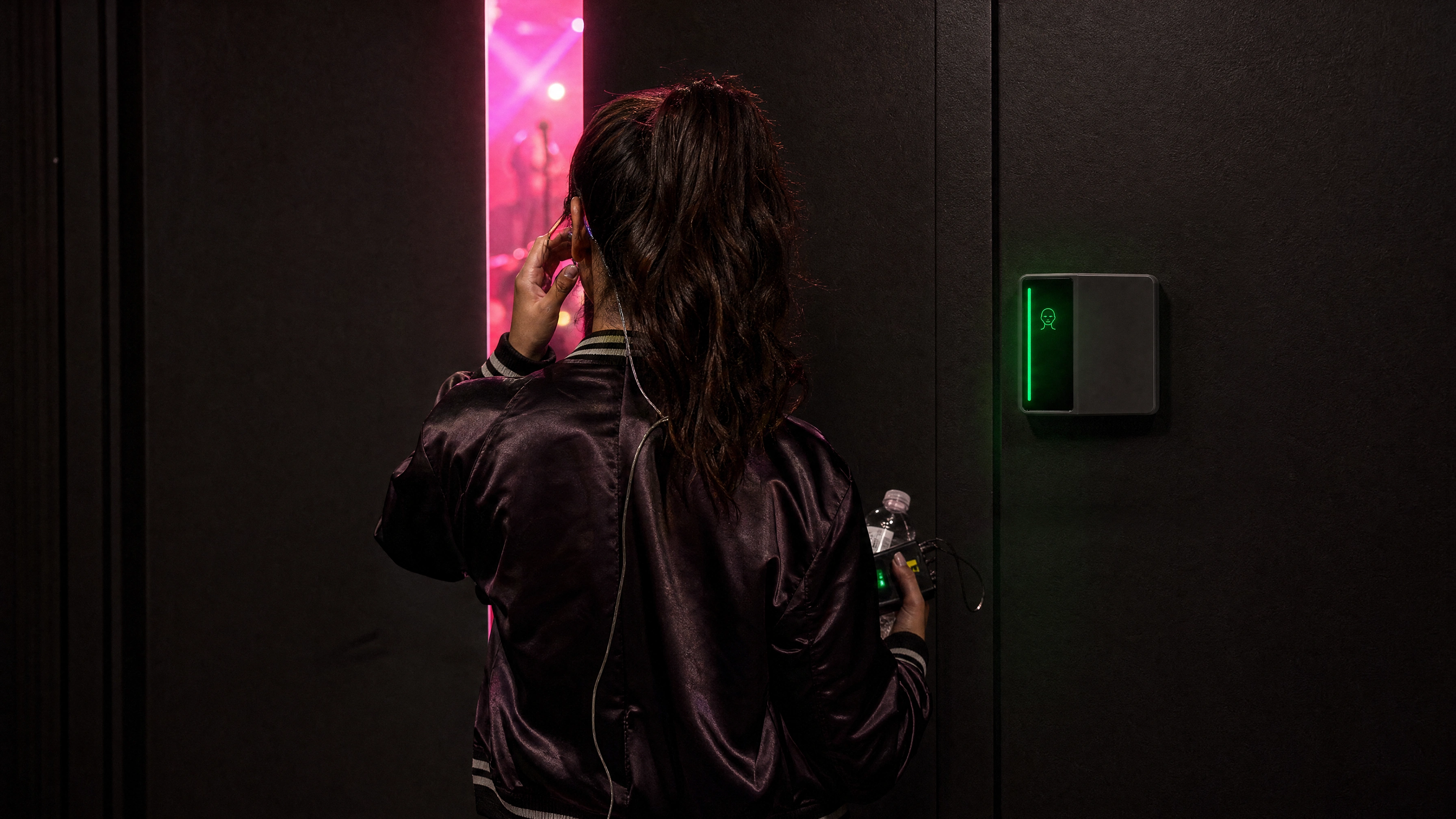 A performer at a backstage door watching the lit stage as the Rock reader beside her turns green