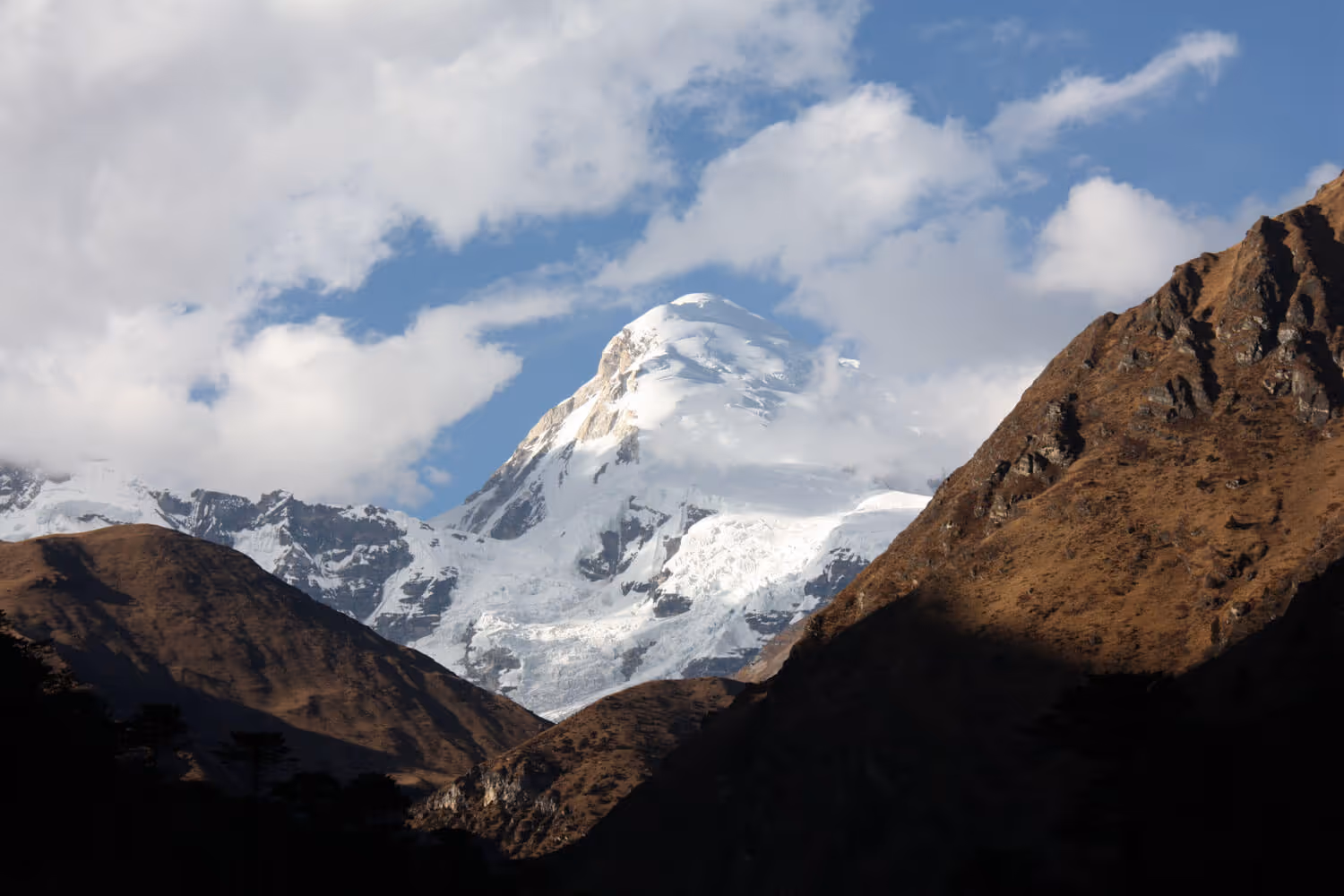 Snow-capped Jomolhari mountain rising above rugged ridges during the Jomolhari trek in Bhutan, under a bright blue sky.