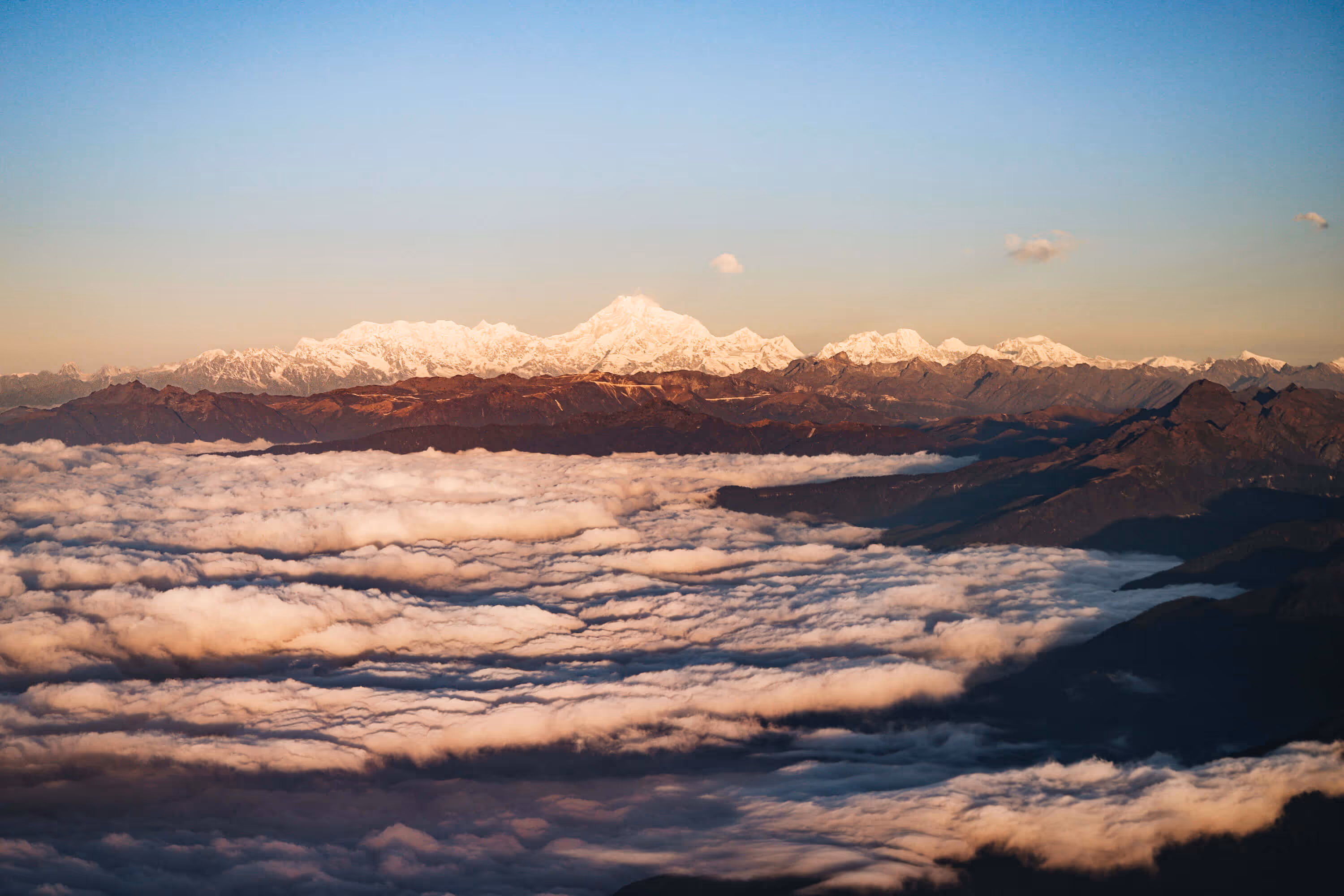 Snow-capped Himalayan peaks glowing above a sea of clouds at sunrise, seen on a scenic flight into Bhutan.