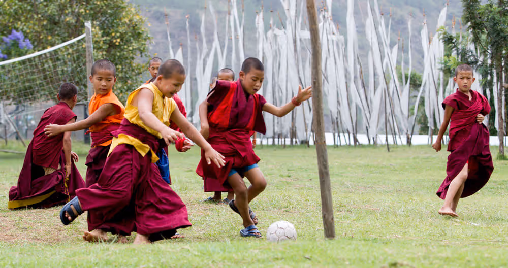 Young monks playing football on a grassy field at Chimi Lhakhang, the Temple of Fertility in Bhutan.