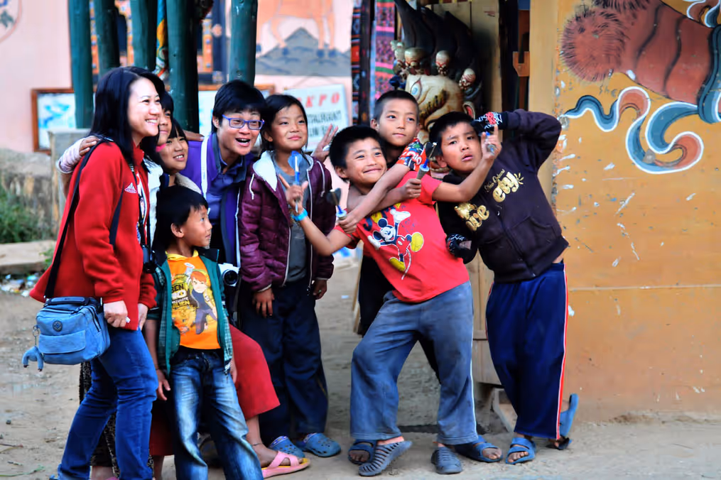 Traveler joyfully posing with a lively group of Bhutanese children, capturing playful energy and local connection.