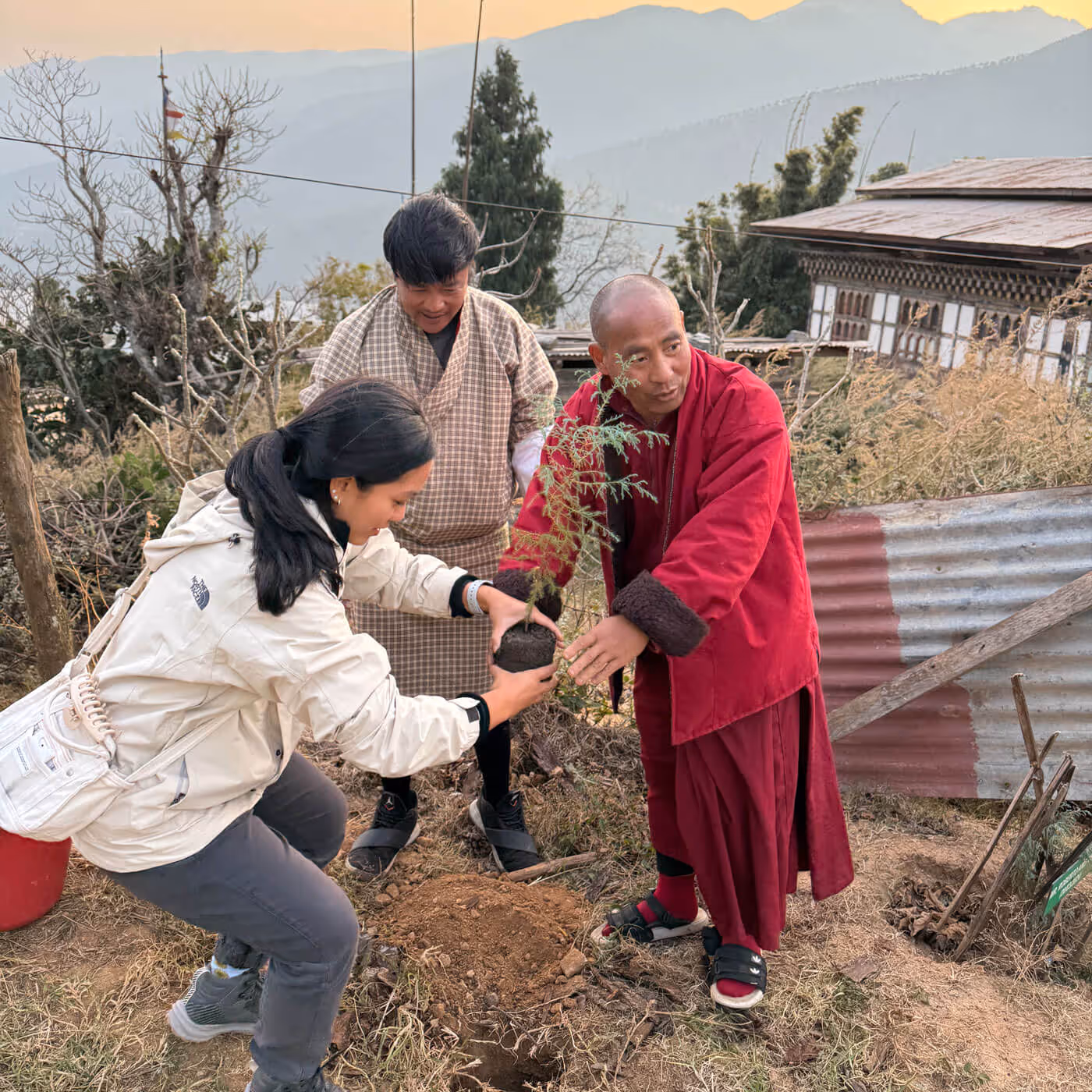 A mindful guest and a Bhutanese monk plant a sapling together, nurturing Bhutan’s forests as part of a meaningful sustainability experience.