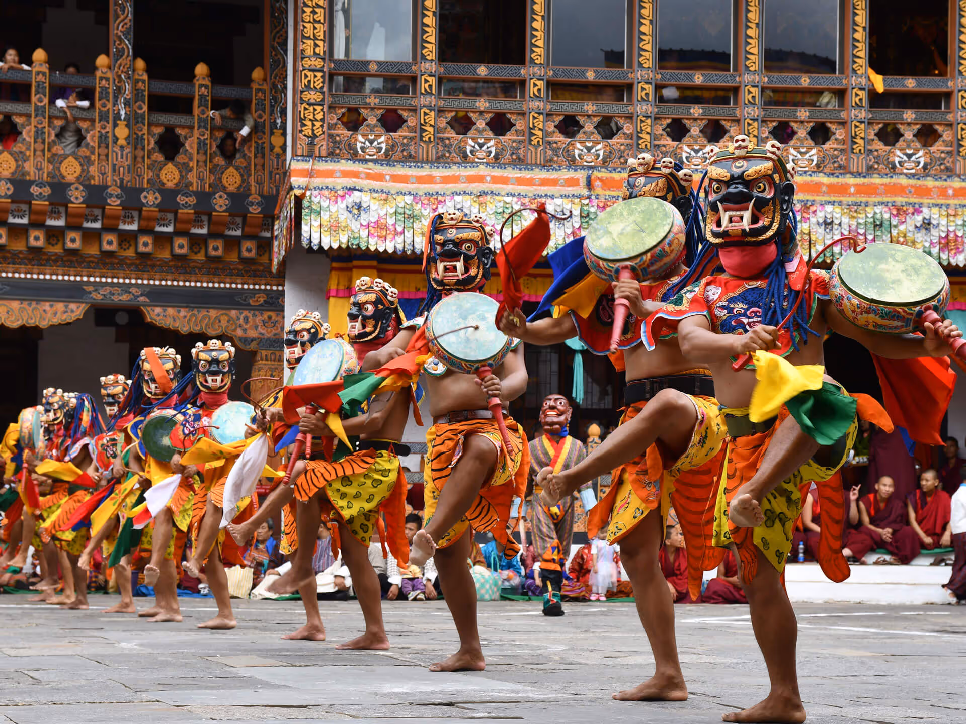 Masked dancers in colorful traditional costumes performing a lively ritual drum dance during the Wangdue Phodrang festival in Bhutan.