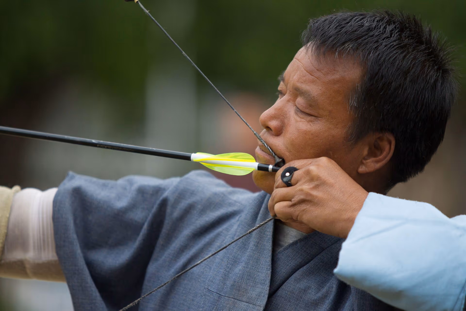 A Bhutanese archer in traditional dress focusing deeply as he draws his bow during an archery competition.