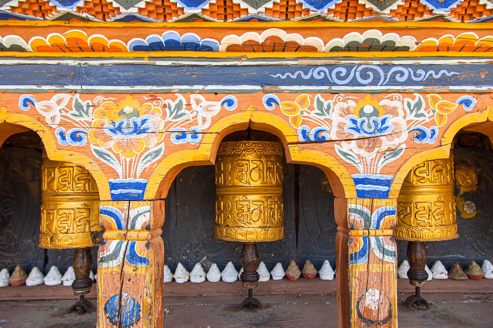 Golden prayer wheels framed by colorful traditional wooden carvings at a monastery in Bhutan.