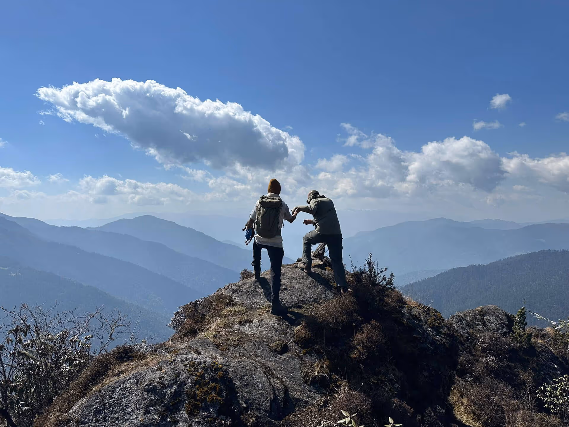 Two trekkers enjoying mountain views during the Druk Path Trek in Bhutan, sharing a joyful moment on the ridge.