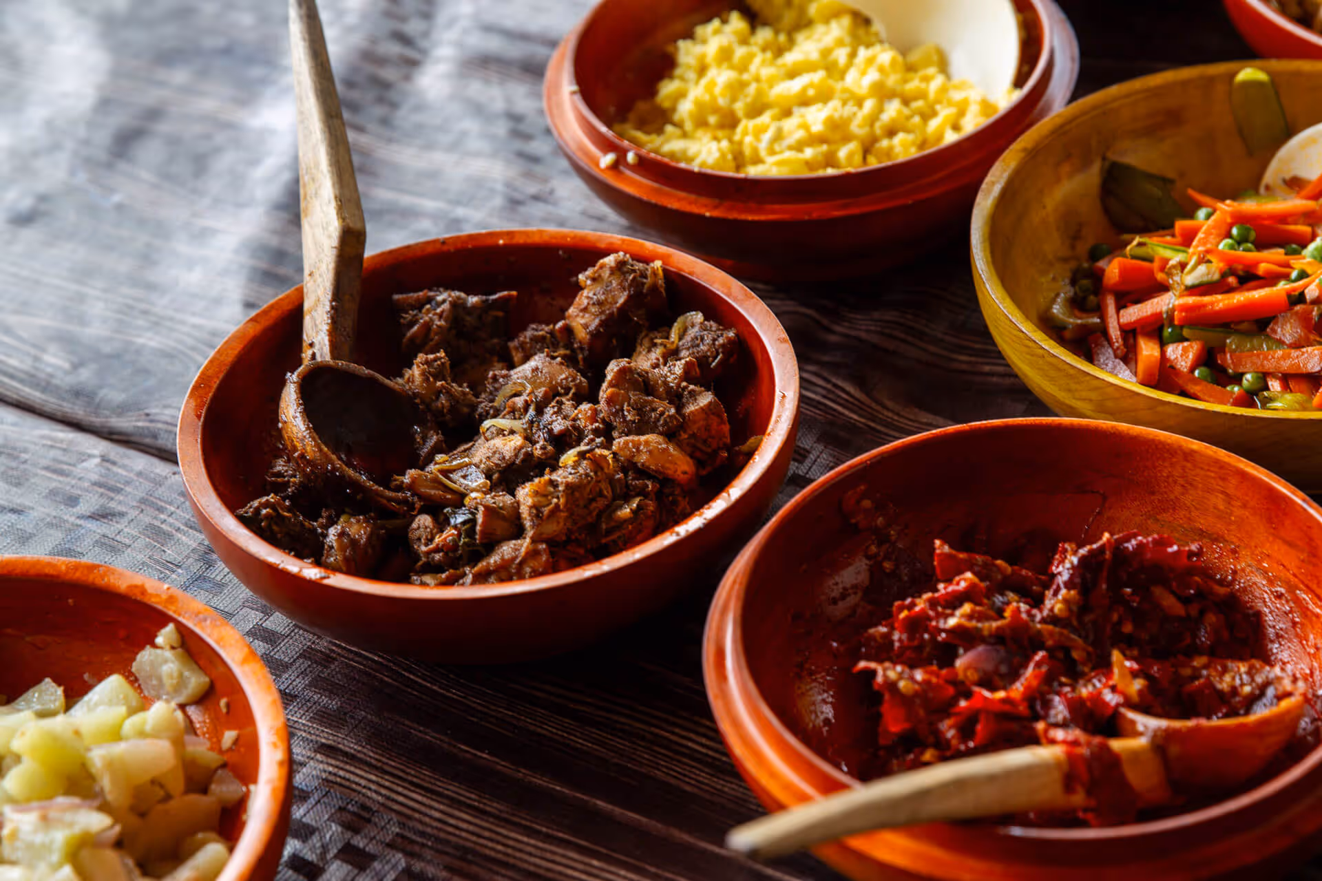 Traditional Bhutanese dishes in wooden bowls, featuring spiced meats and colourful vegetables.