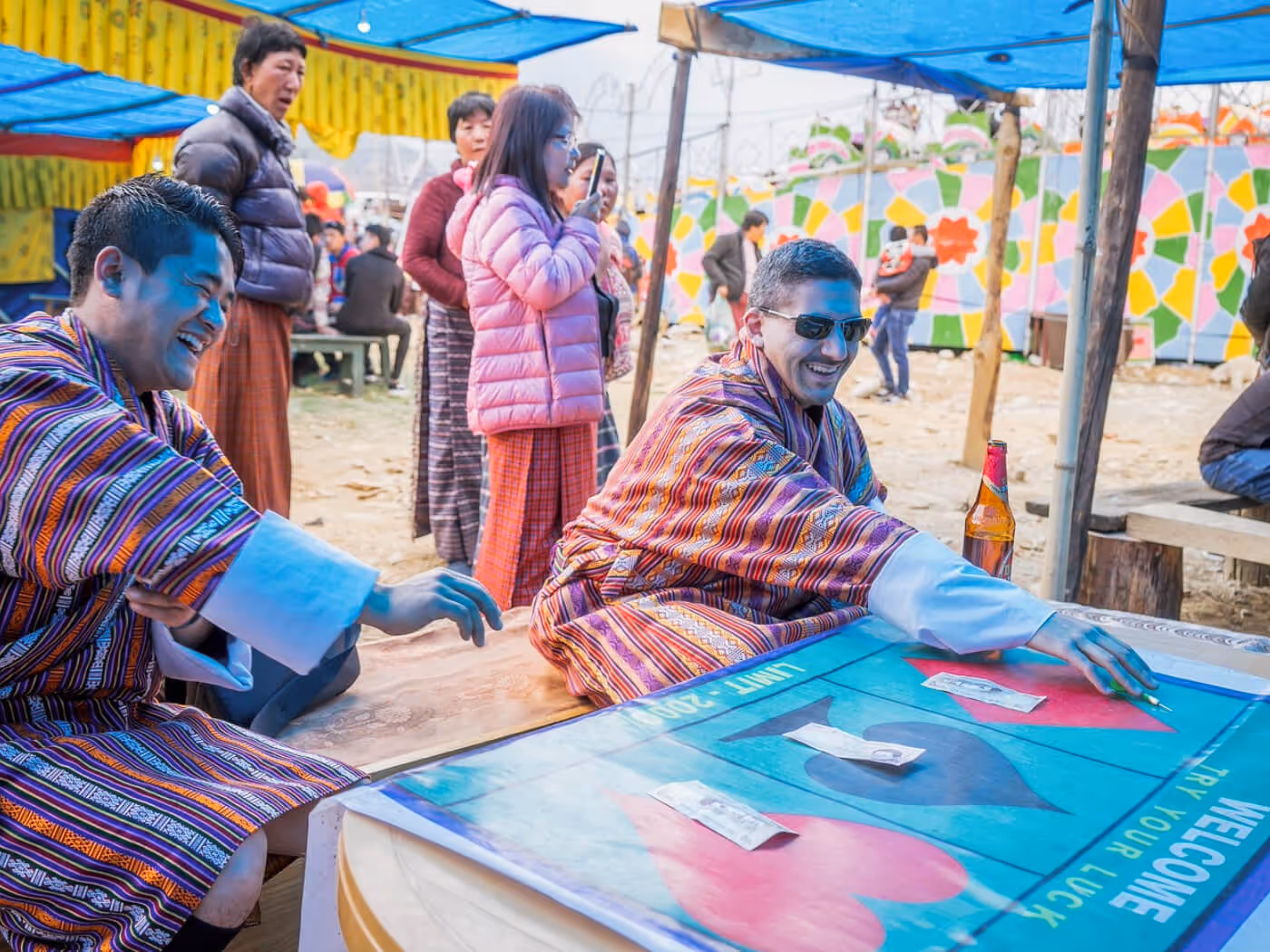 Bhutanese locals and a guest play traditional festival games under vibrant tents, celebrating fun, connection, and community spirit.