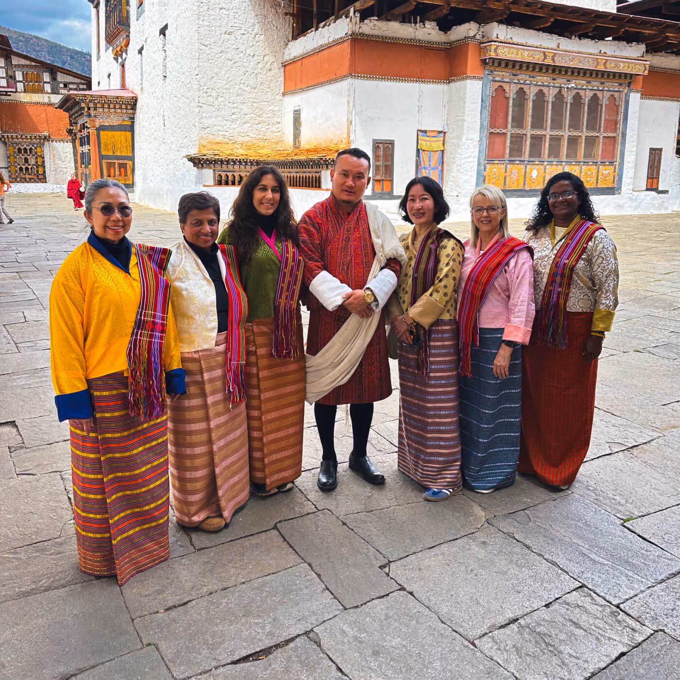 Raven guide standing with guests in kira at dzong courtyard, celebrating cultural immersion in Bhutan.