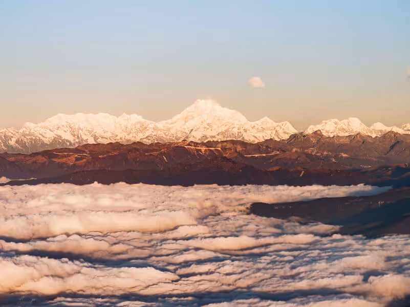 Snow-capped Himalayan peaks glowing above a sea of clouds at sunrise, seen on a scenic flight into Bhutan.