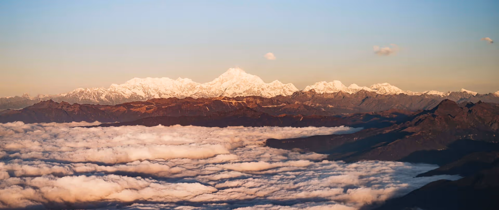 Snow-capped Himalayan peaks glowing above a sea of clouds at sunrise, seen on a scenic flight into Bhutan.