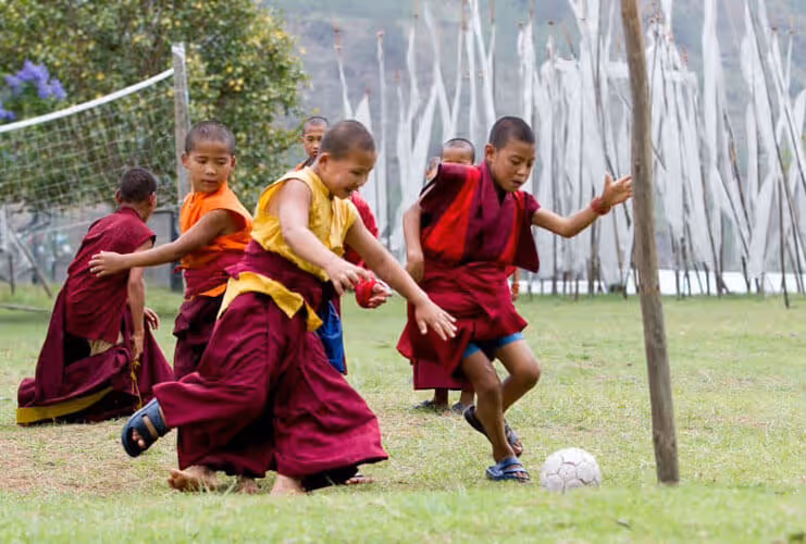 Young monks playing football on a grassy field at Chimi Lhakhang, the Temple of Fertility in Bhutan.