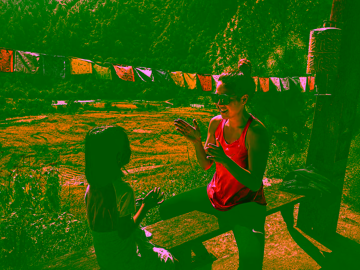A traveller and a Bhutanese girl sharing a conversation beside a valley and prayer flags