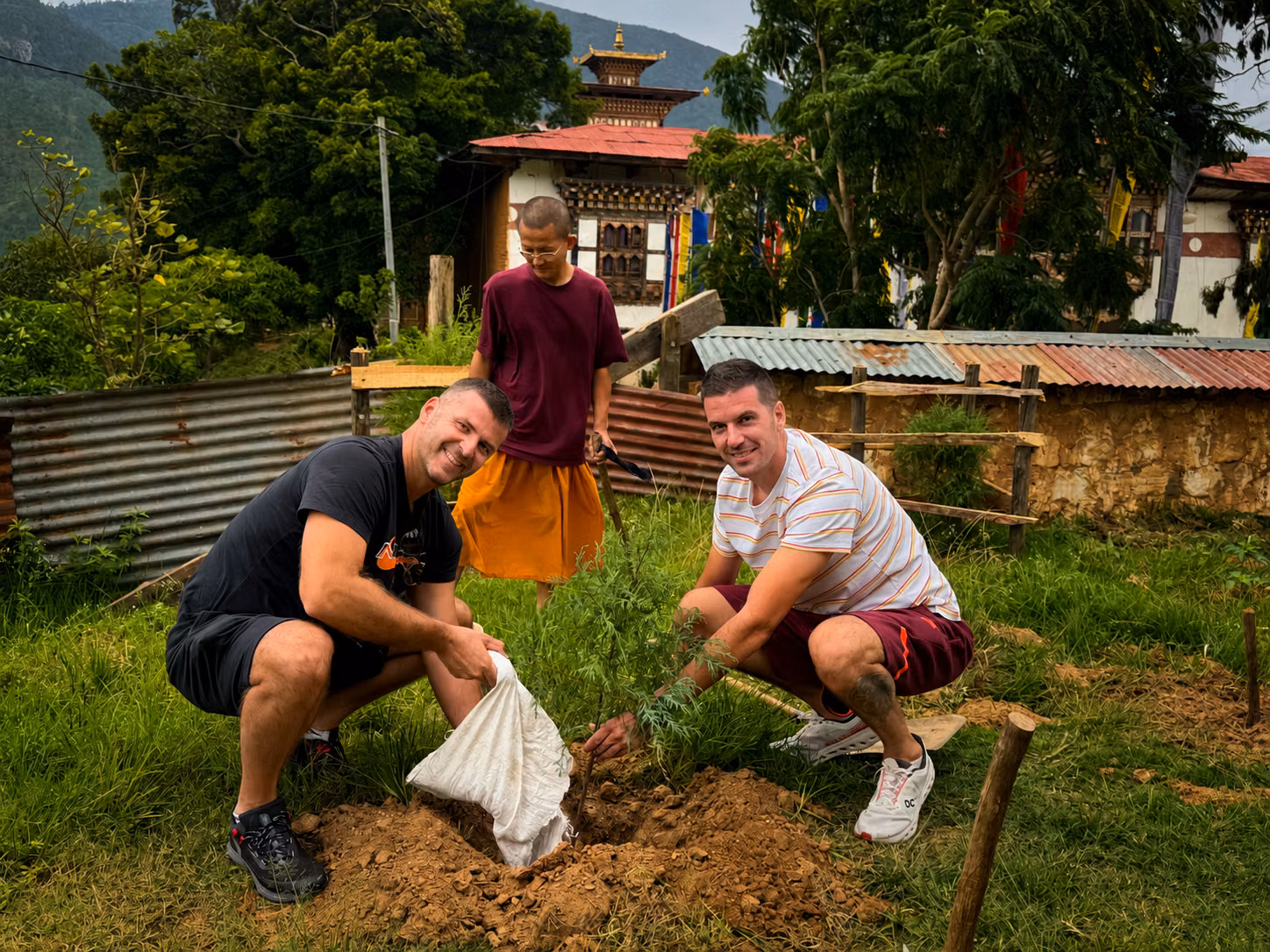 Two Raven guests planting a young tree with a Buddhist monk beside a monastery in Bhutan.