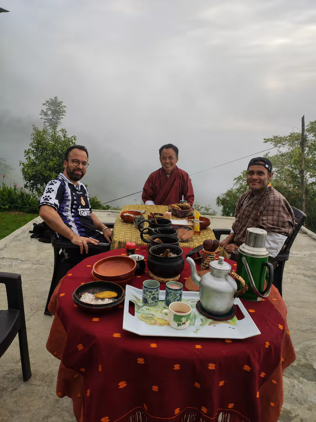 Guests and their Bhutanese guide share breakfast overlooking a misty mountain valley.