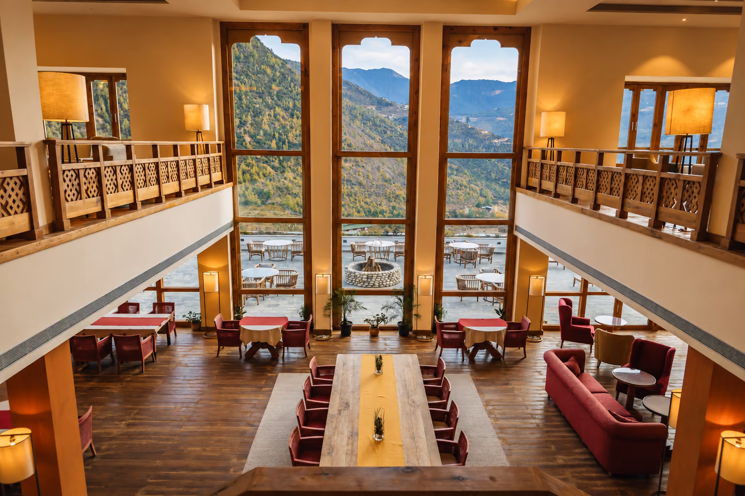 A warm lounge and dining room with tall windows overlooks a mountain valley in Bhutan.
