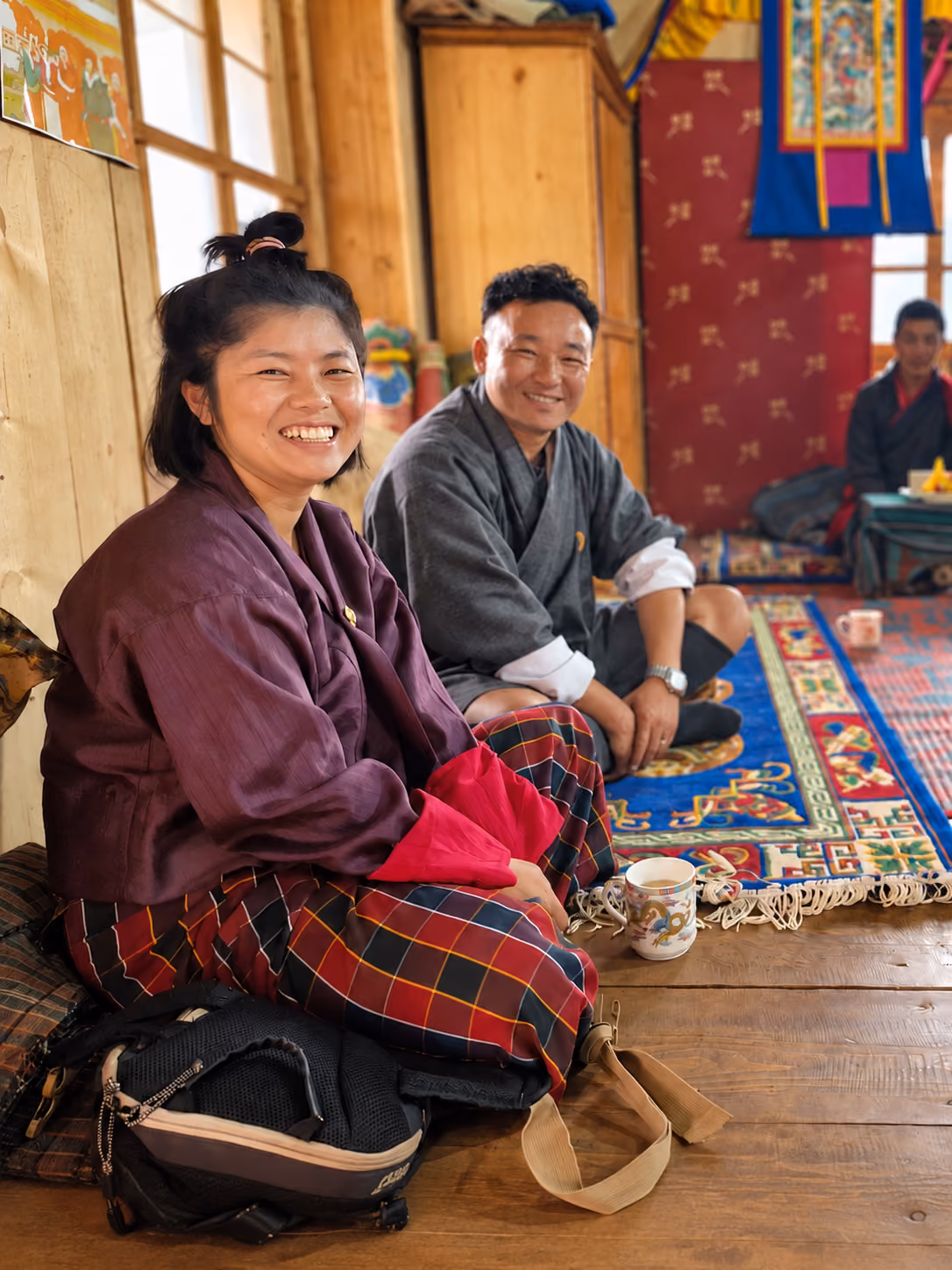 Two people smile together inside a Bhutanese prayer hall.