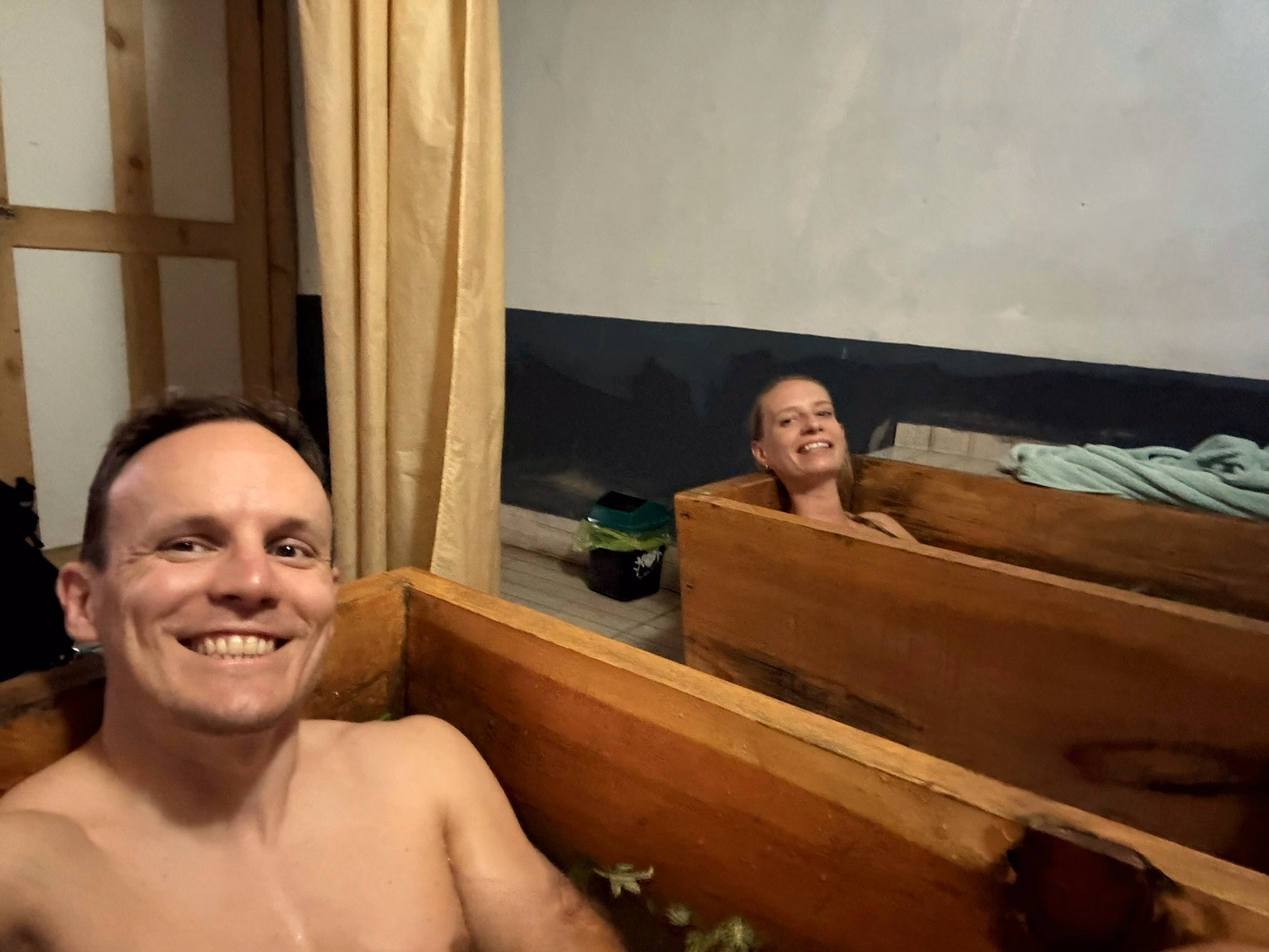 Two guests smiling from traditional wooden hot-stone baths in Paro after trekking in Bhutan.