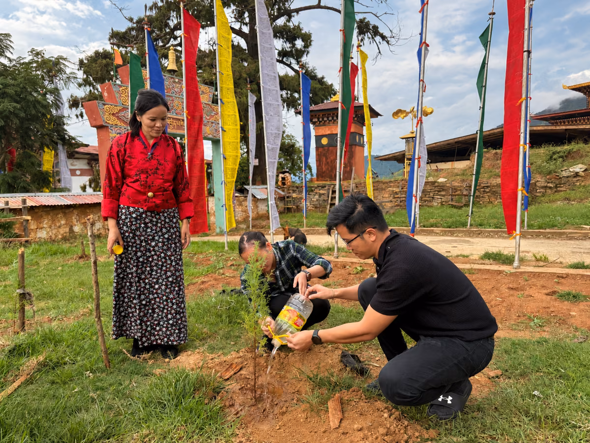Guests watering a young tree among prayer flags at Neyzergang Monastery, Bhutan.
