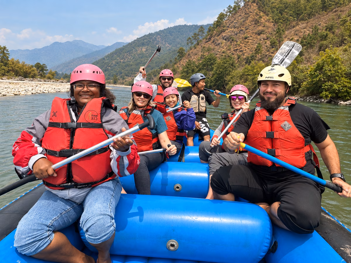 Seven rafters wearing helmets and life jackets aboard a blue raft on the Punakha river.
