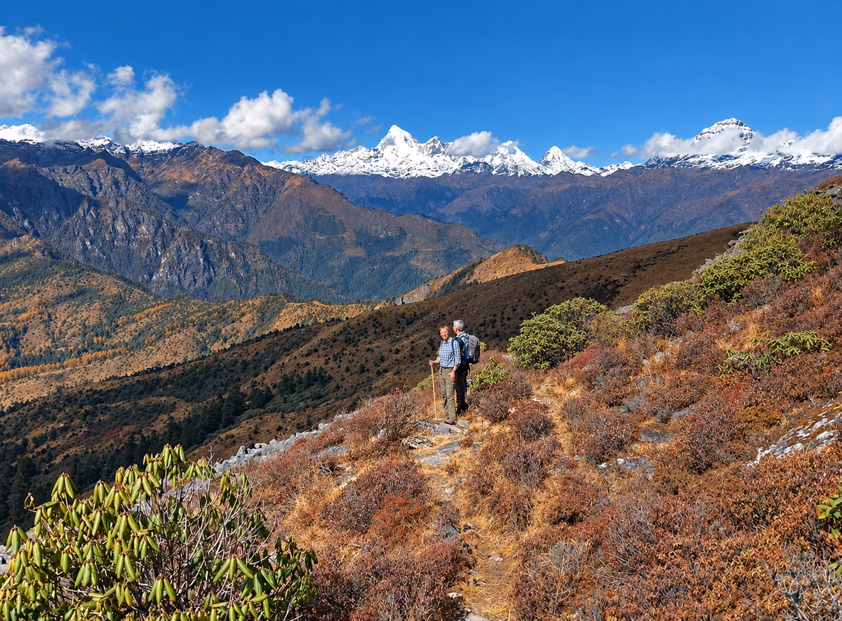 Two trekkers on a highland trail beneath a panorama of snow-covered peaks in Bhutan.