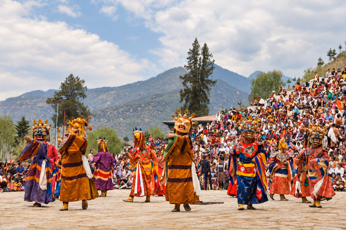 Masked dancers in colourful robes performing before a hillside festival audience in Bhutan.