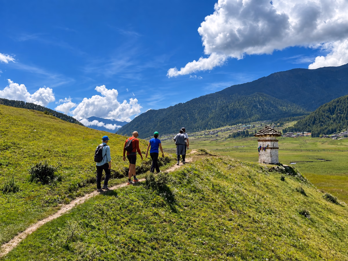 A small group walking along a grassy valley trail beside a chorten in Bhutan.