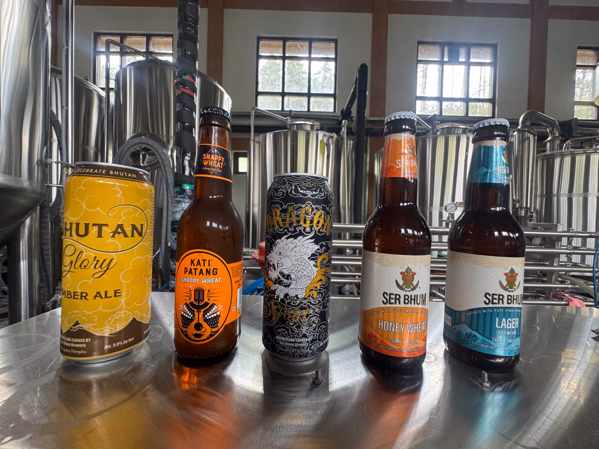 Craft beer bottles and cans displayed in front of brewing tanks at Ser Bhum Brewery, Bhutan.