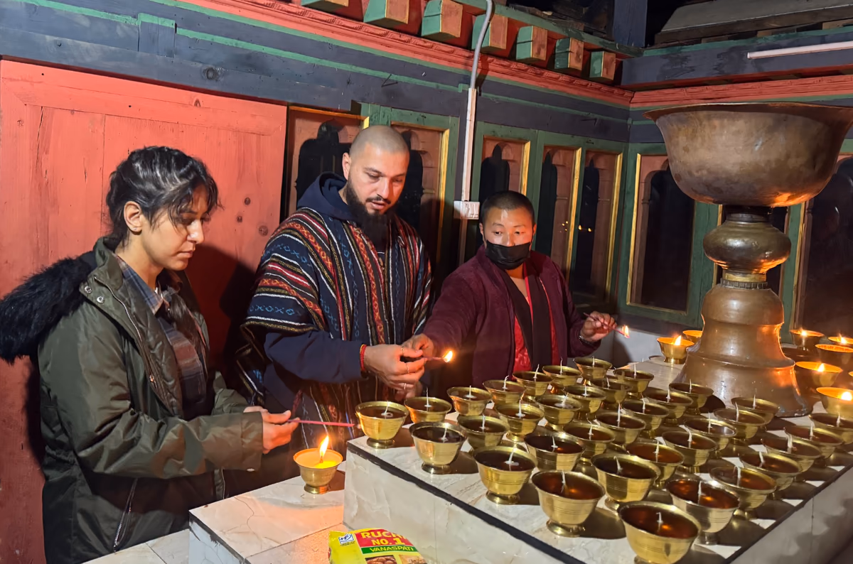 Guests offering butter lamps alongside a monk in a Bhutanese monastery.