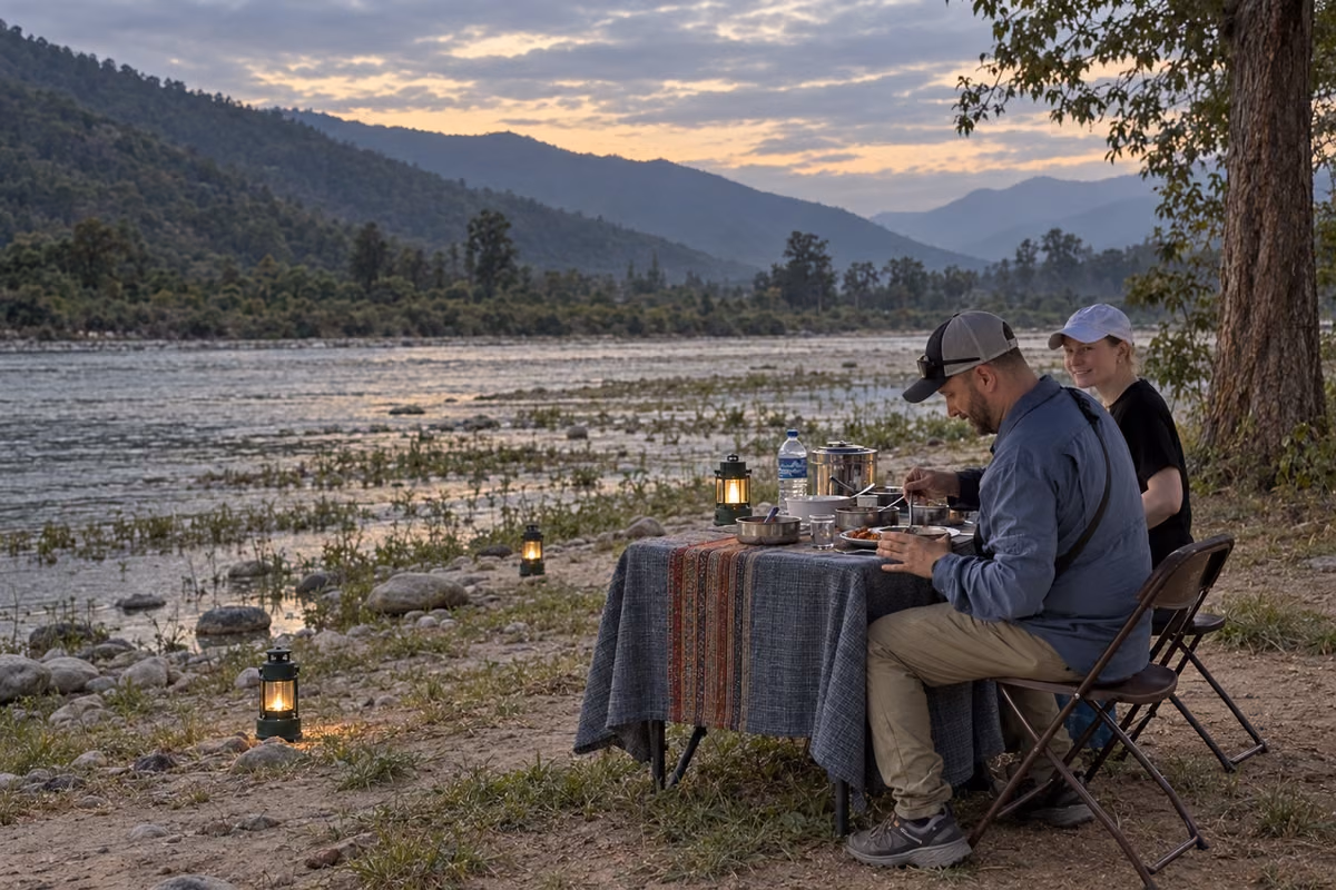Illustration of a couple dining beside a river at dusk with lanterns.