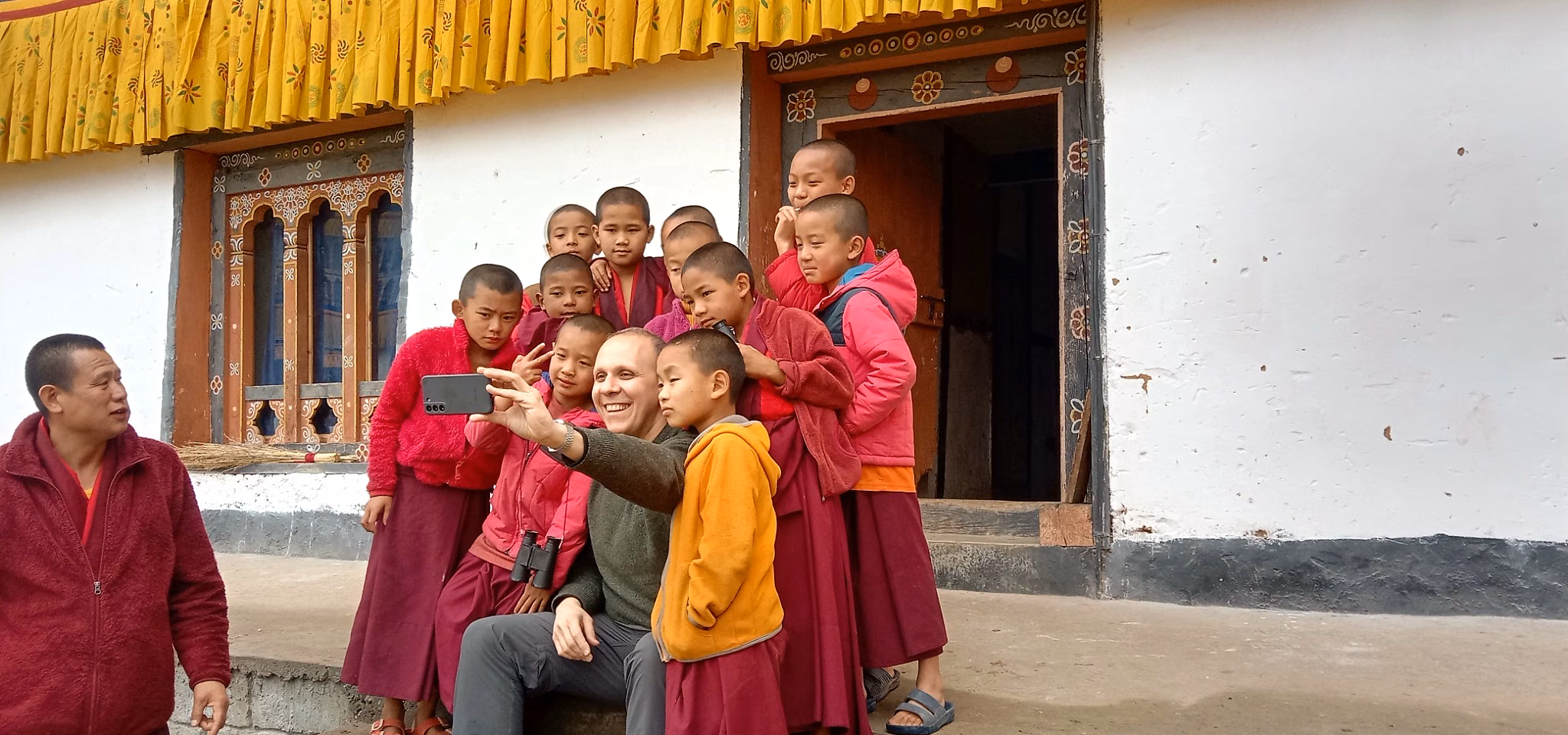 A guest shares a lighthearted moment with young monks outside a monastery in Bhutan.