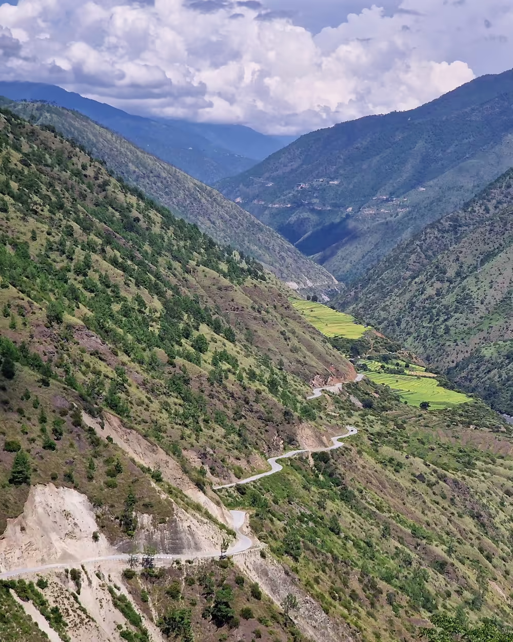 A winding mountain road descends through a river valley on Bhutan’s east-to-west route.
